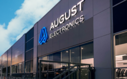 Exterior of August Electronics building with illuminated logo, showcasing modern facility for Electronics Manufacturing Services (EMS) site visits.